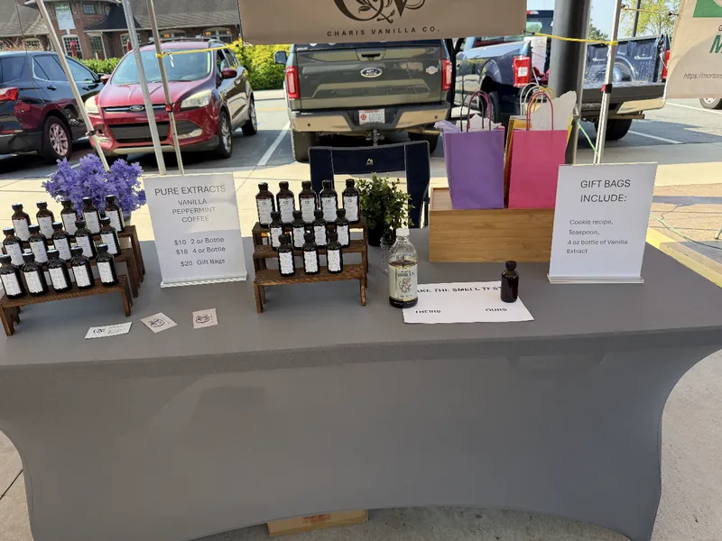 The Charis Vanilla Co. market booth: tiered extract bottles, a price sign, colorful gift bags and the CV banner