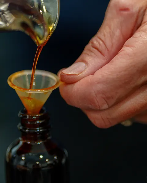 Extract being poured by hand through a small funnel into an amber glass bottle