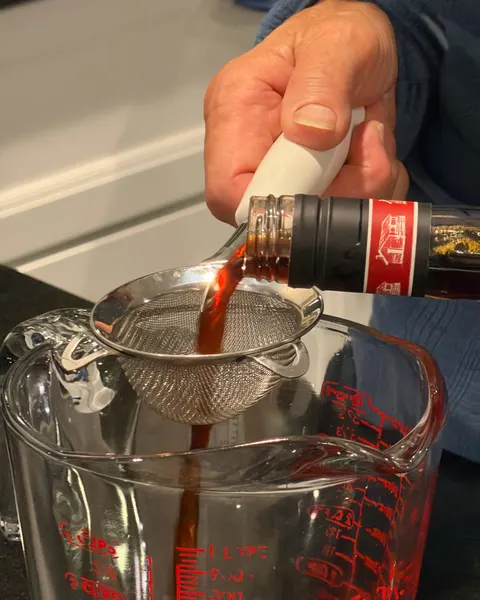 Dark extract being strained through a fine mesh strainer into a glass measuring cup