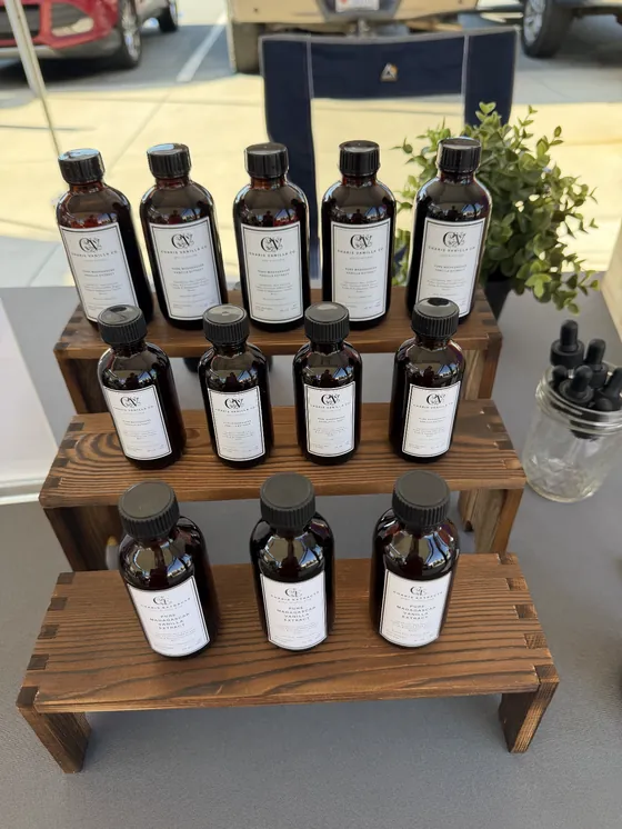 Three wooden tiers of amber Charis extract bottles with black caps beside a small green plant